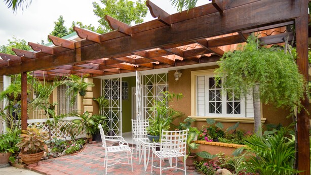 A covered patio with a wooden pergola, potted plants, and white metal chairs. - Centrally Located Guest Apartments II (Kingston)