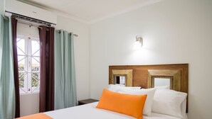 A hotel room with a bed, curtains, a nightstand, and a wall-mounted light fixture. - Centrally Located Guest Apartments II (Kingston)