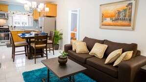 A modern kitchen with wooden cabinets, a dining area with a table and chairs, a brown sofa with cushions, and a painting on the wall. - Centrally Located Guest Apartments II (Kingston)