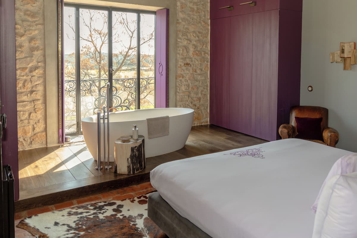 A bedroom with a large bed, a bathtub, and a stone wall.