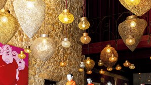 Ein Restaurantinneres mit Steinwänden, herzförmigen Pendelleuchten und Statuen von Mönchen.