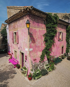 A pink building with a sign reading 'LA PETIT TABLE,' a street lamp, and potted plants. - Village Castigno - Wine hotel & resort (Assignan)