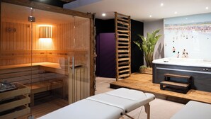 Ein Sauna-Raum mit Glasabtrennung, einer Holzbank und einem Massagetisch.