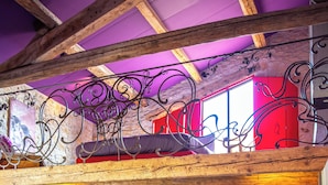 Ein Wohnbereich im Loft-Stil mit freiliegenden Holzbalken, einer Steinwand und einer Farbgestaltung in Rot und Violett.
