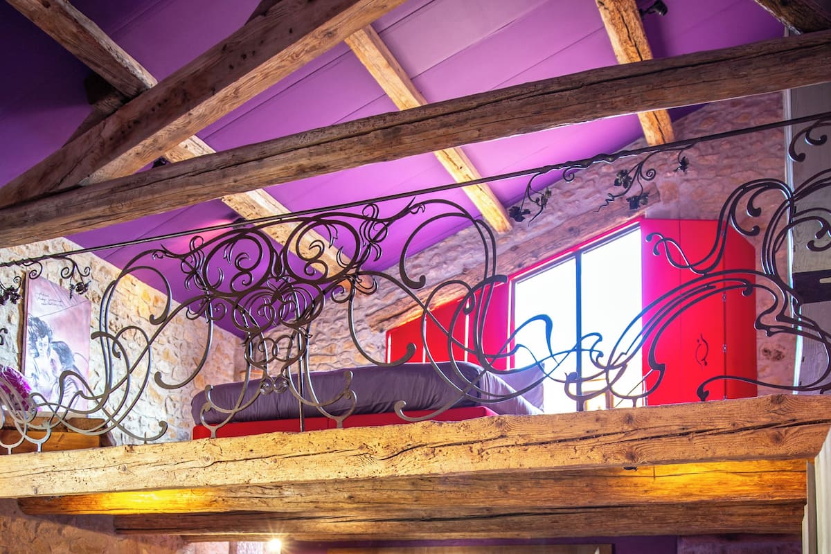 A loft-style living area with exposed wooden beams, a stone wall, and a red and purple color scheme.