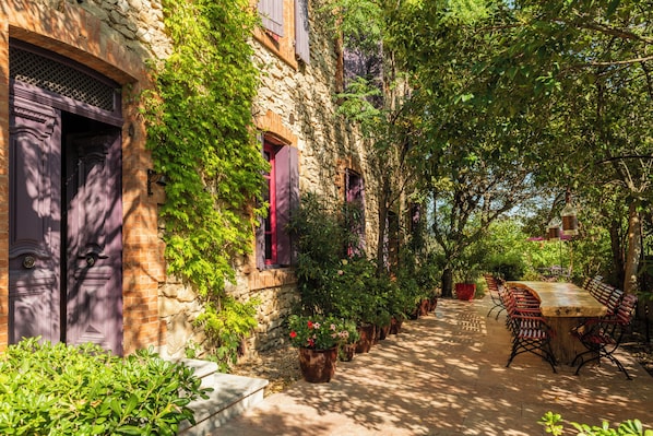 A stone building with a wooden door, potted plants, and a table with chairs. - Village Castigno - Wine hotel & resort (Assignan)