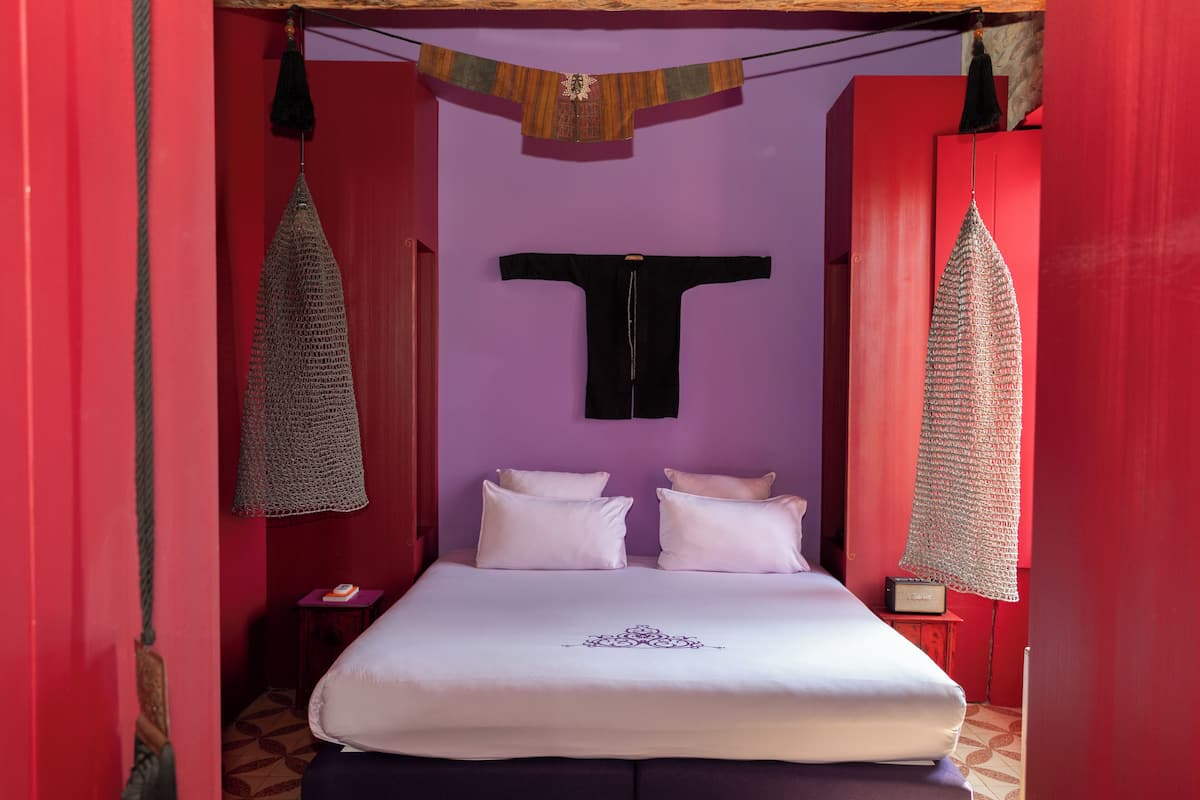 A room with a bed, pillows, a hanging textile, and a wall-mounted T-shirt.