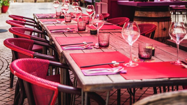 Ein Restaurant mit Außenbereich, roten Sonnenschirmen und Weingläsern auf den Tischen.