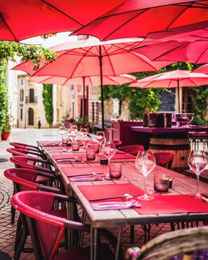 A restaurant with outdoor seating, red umbrellas, and wine glasses on tables. - Village Castigno - Wine hotel & resort (Assignan)