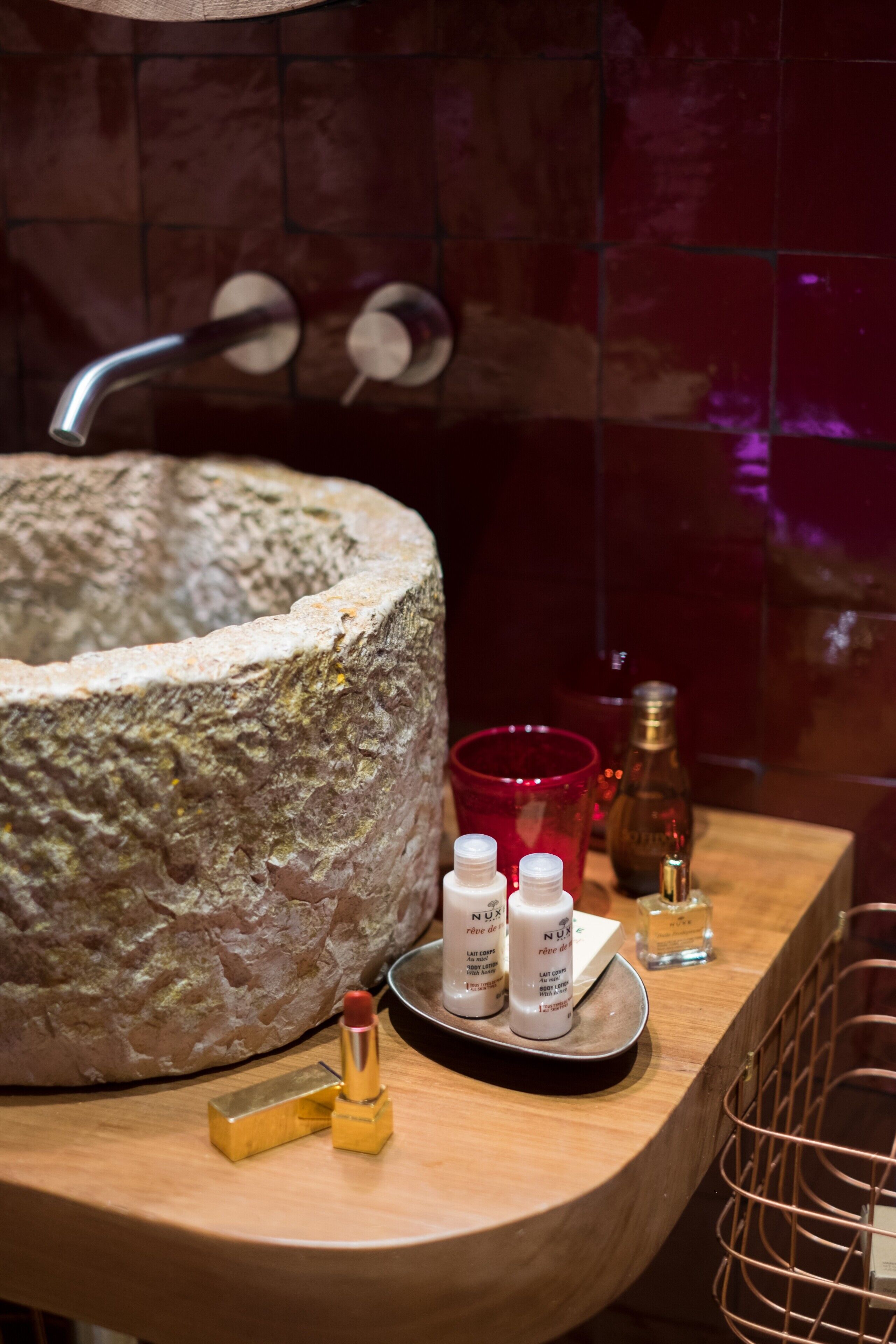 A bathroom with a stone sink, a red glass, and various toiletries on a tray.