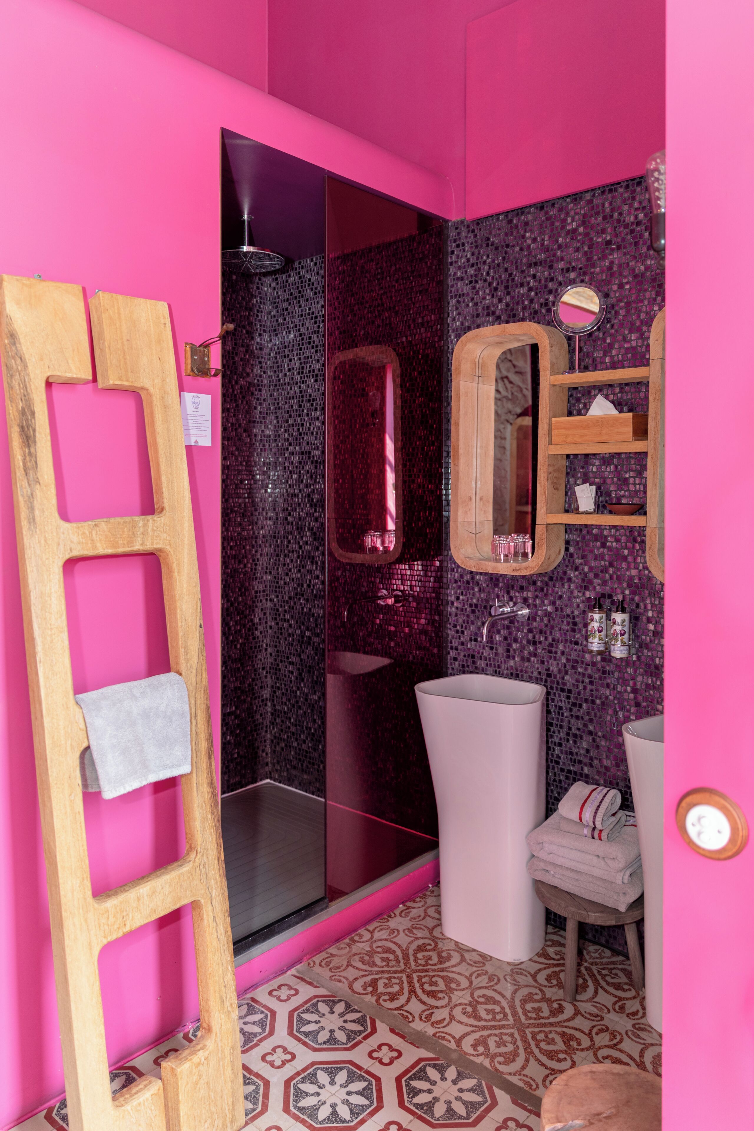 Une salle de bain avec un mur rose, une douche, un lavabo et un miroir.