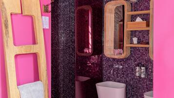 Une salle de bain avec un mur rose, une douche, un lavabo et un miroir.