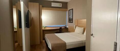 Habitación de hotel moderna con piso de madera, una cama con cabecera, un escritorio con silla, un espejo y un aire acondicionado instalado en la pared.