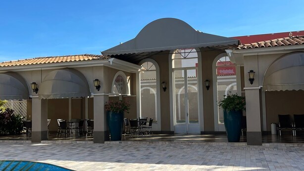 Un área de piscina con solárium empedrado, mobiliario exterior y un porche cubierto.