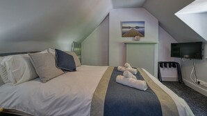 A hotel room with a bed, towels, a television, and a painting on the wall. - Woodlands Bed & Breakfast (Dornoch)