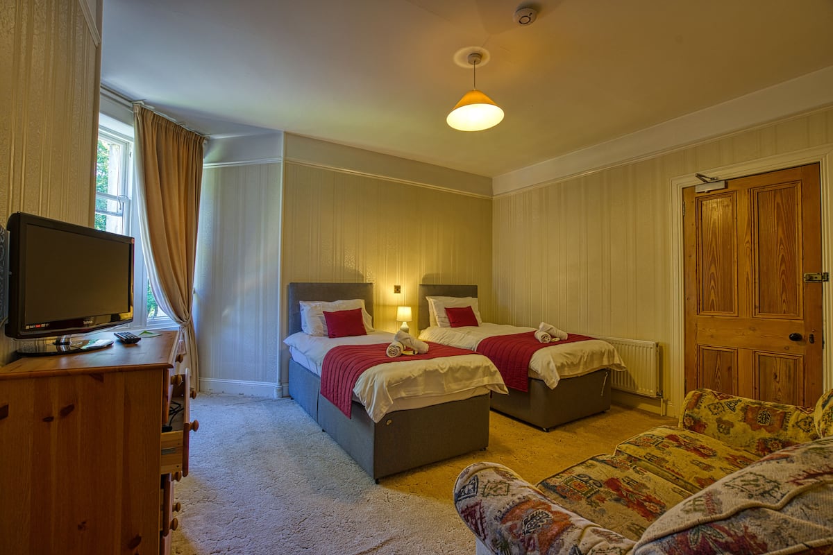 A hotel room with two beds, a television, a sofa, and a wooden door.