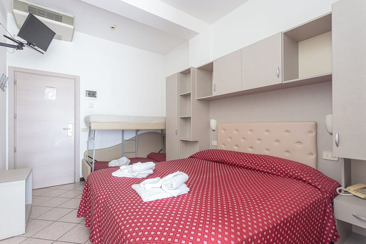 Habitación de hotel con cama, escritorio, silla, armario, espejo y teléfono.