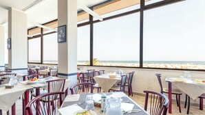 A restaurant with tables set for dining, large windows with a beach view, and a casual dining atmosphere. - Hotel Blumen (Rimini)