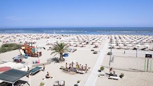 A beach with numerous umbrellas and sun loungers, a playground, and a clear view of the sea. - Hotel Blumen (Rimini)