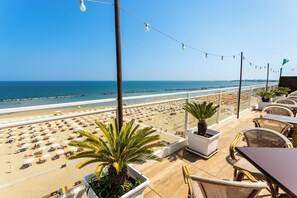 Une terrasse au bord de la plage, avec des sièges en plein air, une vue sur la plage et un palmier.