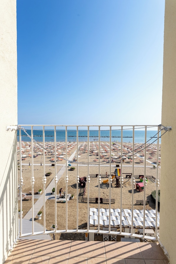 Un balcon donnant sur une plage, avec des transats et des parasols.