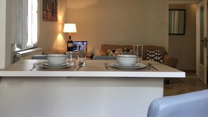 A dining area with a table set for two, a television in the background, and a sofa with patterned cushions. - Helios (Florence)