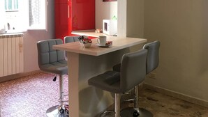 A modern kitchen with a red cabinet, a white countertop, and two bar stools. - Helios (Florence)