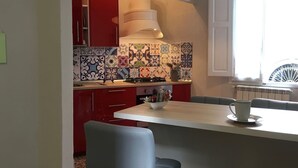 A compact kitchen with red cabinets, a white countertop, and a variety of colorful tiles. - Helios (Florence)