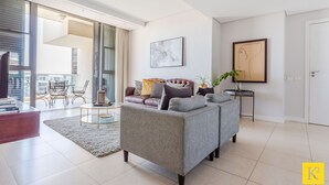 A modern living room with a grey sofa, a coffee table, and a dining area with wicker chairs. - 606 Juliette B (Cape Town)