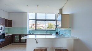 A modern kitchen with a large island, two bar stools, and a view of buildings through the window. - 606 Juliette B (Cape Town)