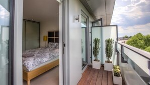 A modern bedroom with a wooden bed, a glass door leading to a balcony with potted plants.