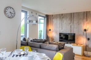 A modern living room with a sofa, TV, and dining area with chairs and table.