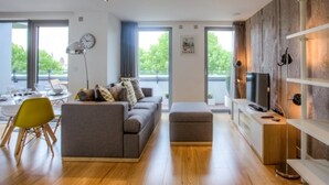 A modern living room with a sofa, ottoman, and a television. There is a dining area with a table and chairs.