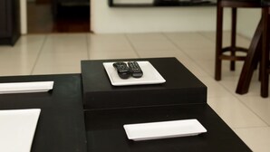 A modern hotel room with a black desk, a bed, and a TV mounted on the wall.