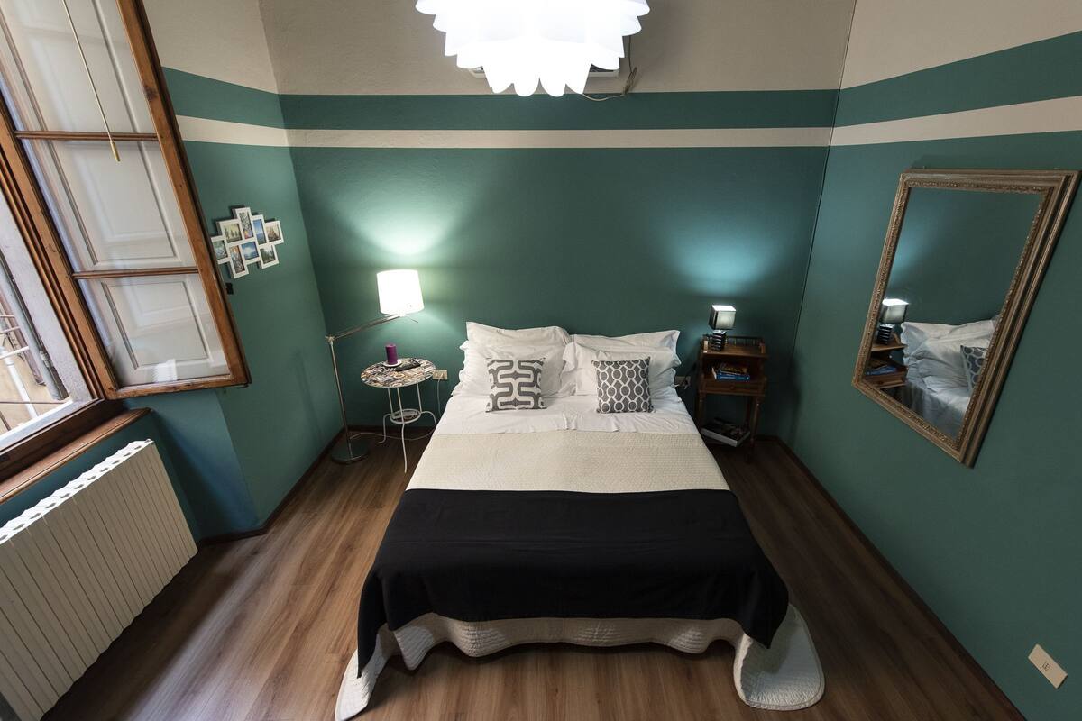 A bedroom with a bed, bedside tables, a mirror, and a window.