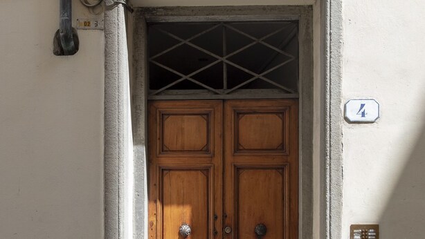 A double wooden door with a metal grid above it, set in a concrete frame. - Luna (Florence)
