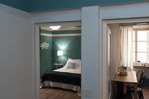 A bedroom with a bed, bedside table, lamp, and a view of a dining area with a table and chairs. - Luna (Florence)