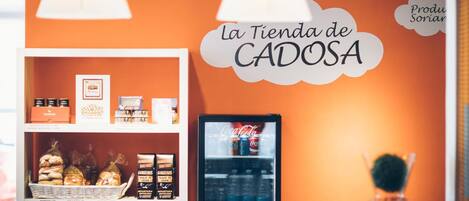 A bakery counter with a sign reading "La Tienda de CADOSA" and a refrigerator stocked with beverages.