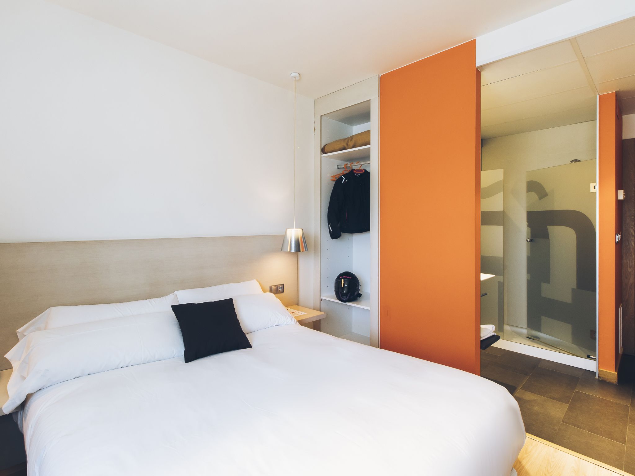 Une chambre d’hôtel avec un lit, une table de chevet, une armoire et une salle de bain visible à travers une porte ouverte.
