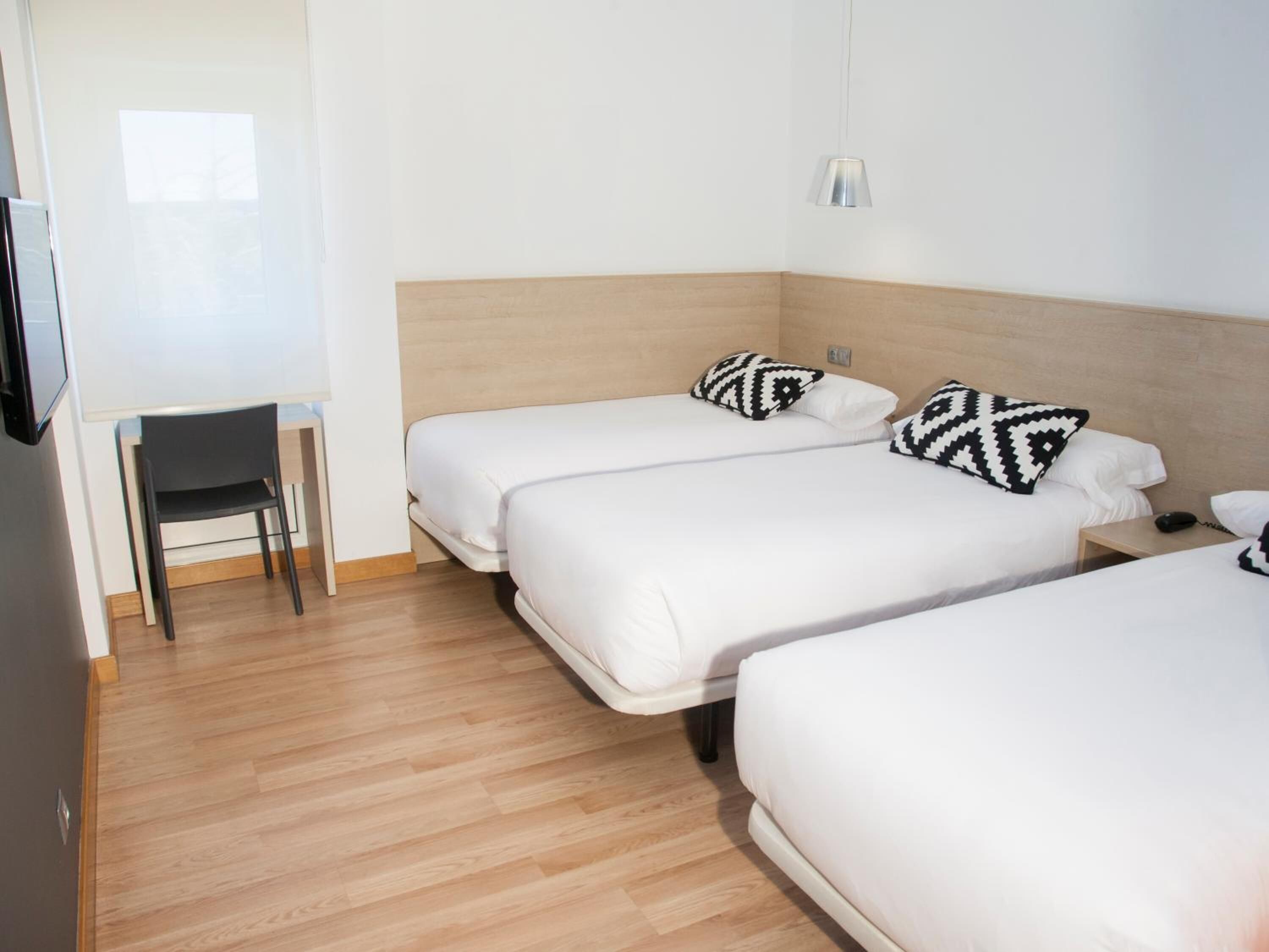 A hotel room with two beds, a desk, and a chair.