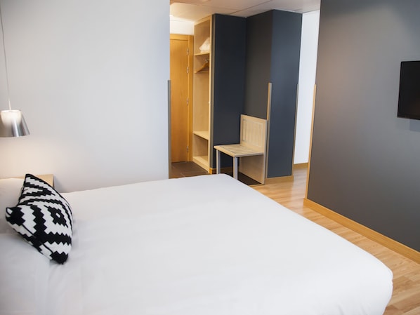 A hotel room with a bed, a bedside lamp, a chair, a wardrobe, and a television. - Hotel Cadosa (Soria)
