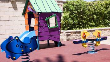 A playground with a purple playhouse, a blue slide, and yellow seesaw.