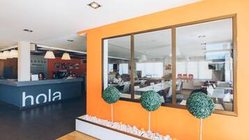 Een modern interieur met een receptiebalie, een grote spiegel en een zithoek met tafels en stoelen.