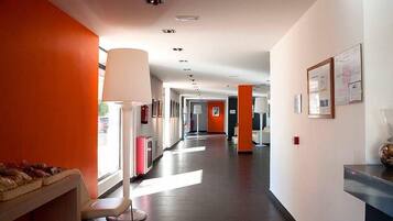 Un pasillo moderno de hotel con una pared naranja brillante, una recepción y una zona de estar con una lámpara.