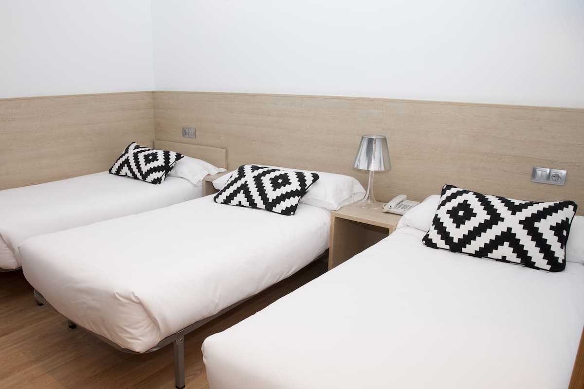 Dos camas individuales con sábanas blancas y almohadas con estampado blanco y negro, una mesita de noche con lámpara y teléfono, y un cabecero de madera.