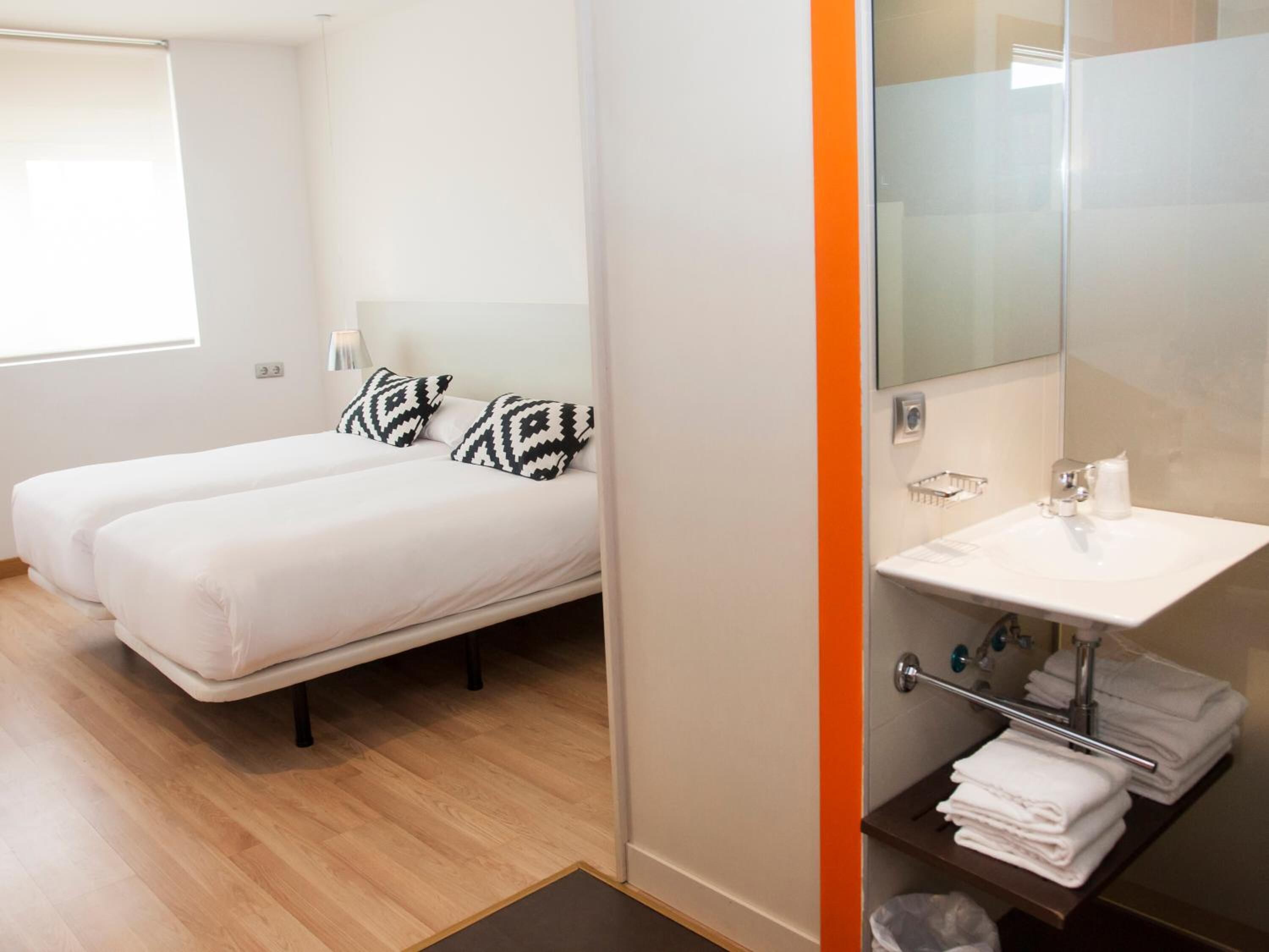 Habitación de hotel con dos camas, baño con lavamanos y toallero, y ventana con persianas.