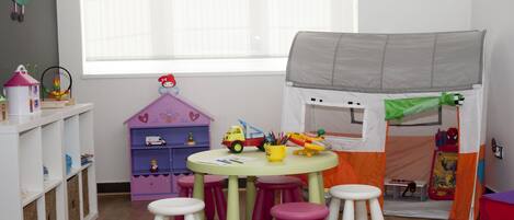 Una sala de juegos infantil con una tienda de campaña, una mesa con taburetes y una casita de juguete.