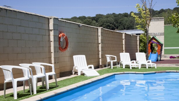 A swimming pool with white lounge chairs and a lifebuoy on a brick wall. - Hotel Cadosa (Soria)