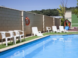 A swimming pool with white lounge chairs and a lifebuoy on a brick wall.