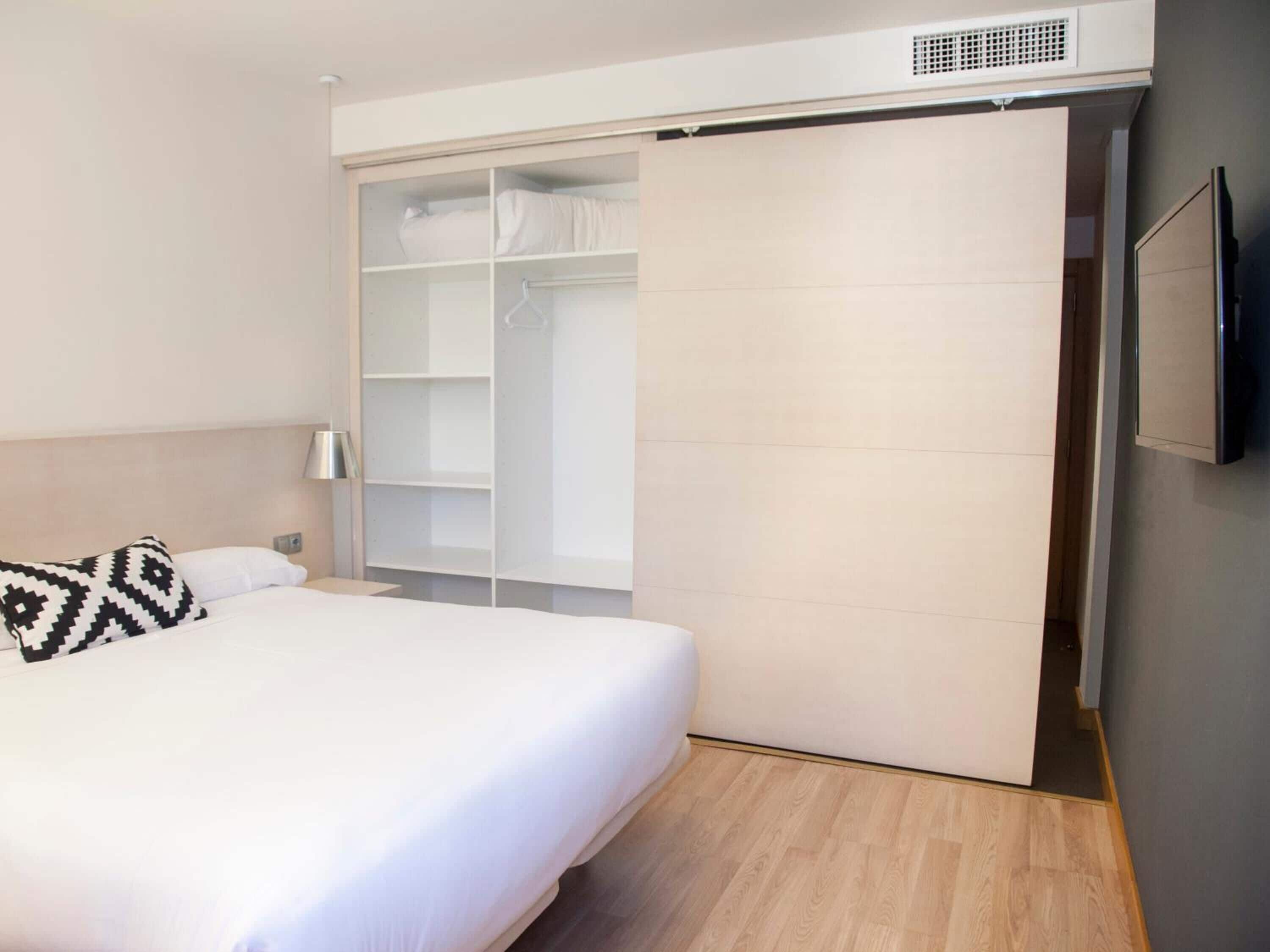 Een slaapkamer met een bed, een kledingkast, een televisie en een nachtkastje.
